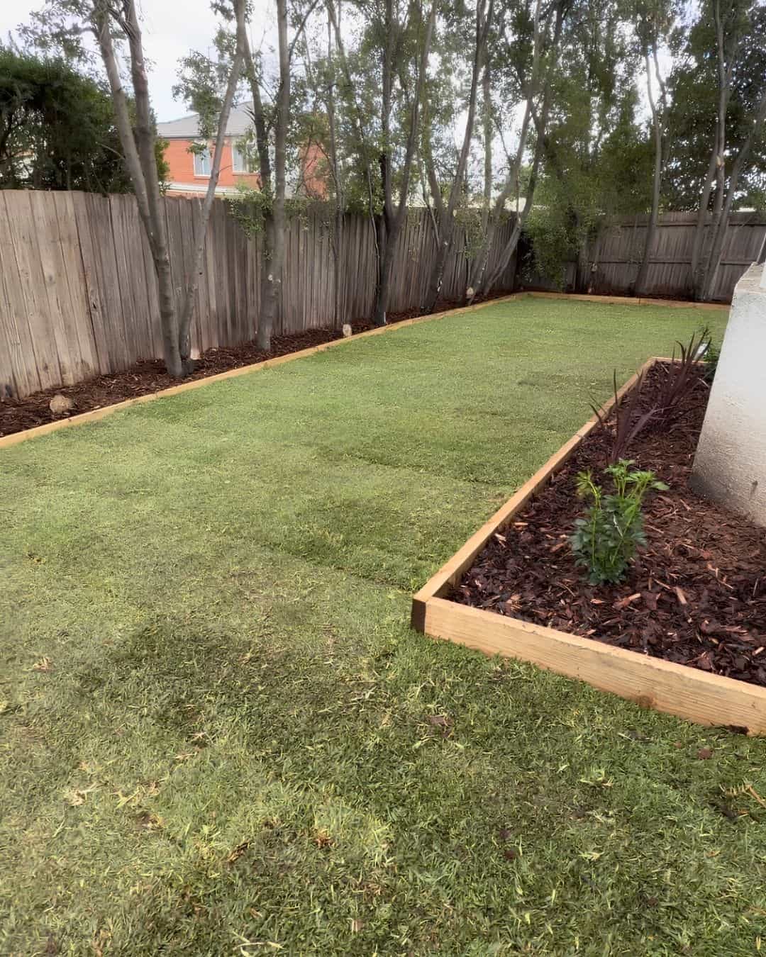Completed Hillside backyard with fresh lawn, timber-edged garden beds, mulch and new planting around existing trees