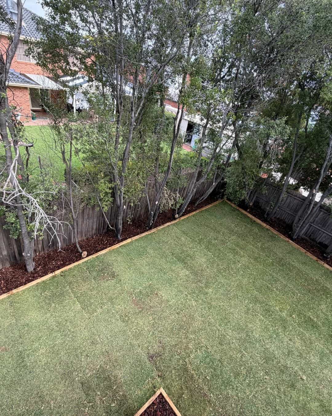 Wide view of a landscaped Hillside backyard with newly laid turf and mulched garden borders along the fence line