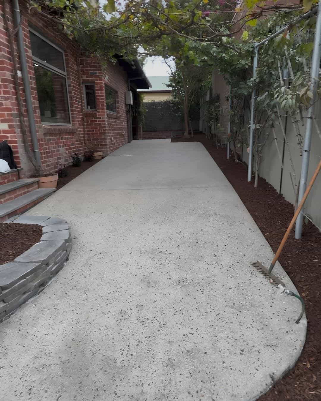 Finished side access in Templestowe Lower with exposed aggregate concrete, mulched garden beds and stone edging beside the brick home
