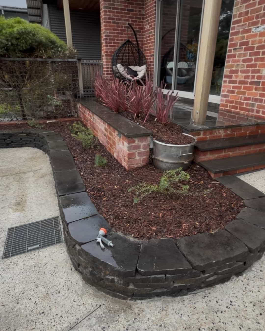 Landscaped garden bed in Templestowe Lower with dark stone edging, fresh mulch and feature planting beside the patio