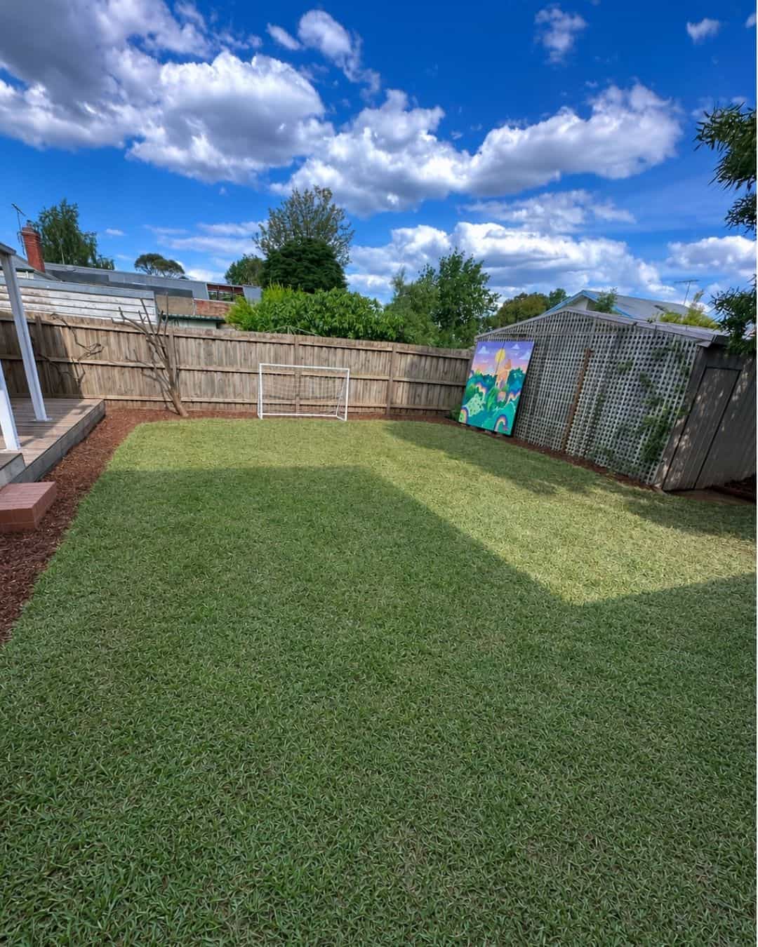 Finished backyard in Northcote with newly laid lawn and mulched garden edges around existing trees and fencing